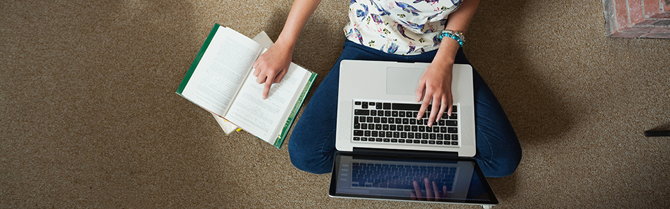 Female sitting on floor with laptop and books.