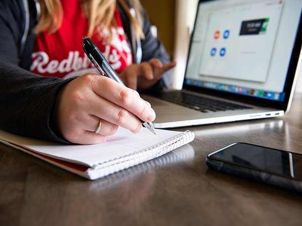 Female sitting with close-up of laptop and notebook.